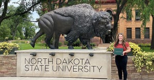Sarah McNaughton hoklding diploma next to North Dakota State University sign and buffalo sculpture