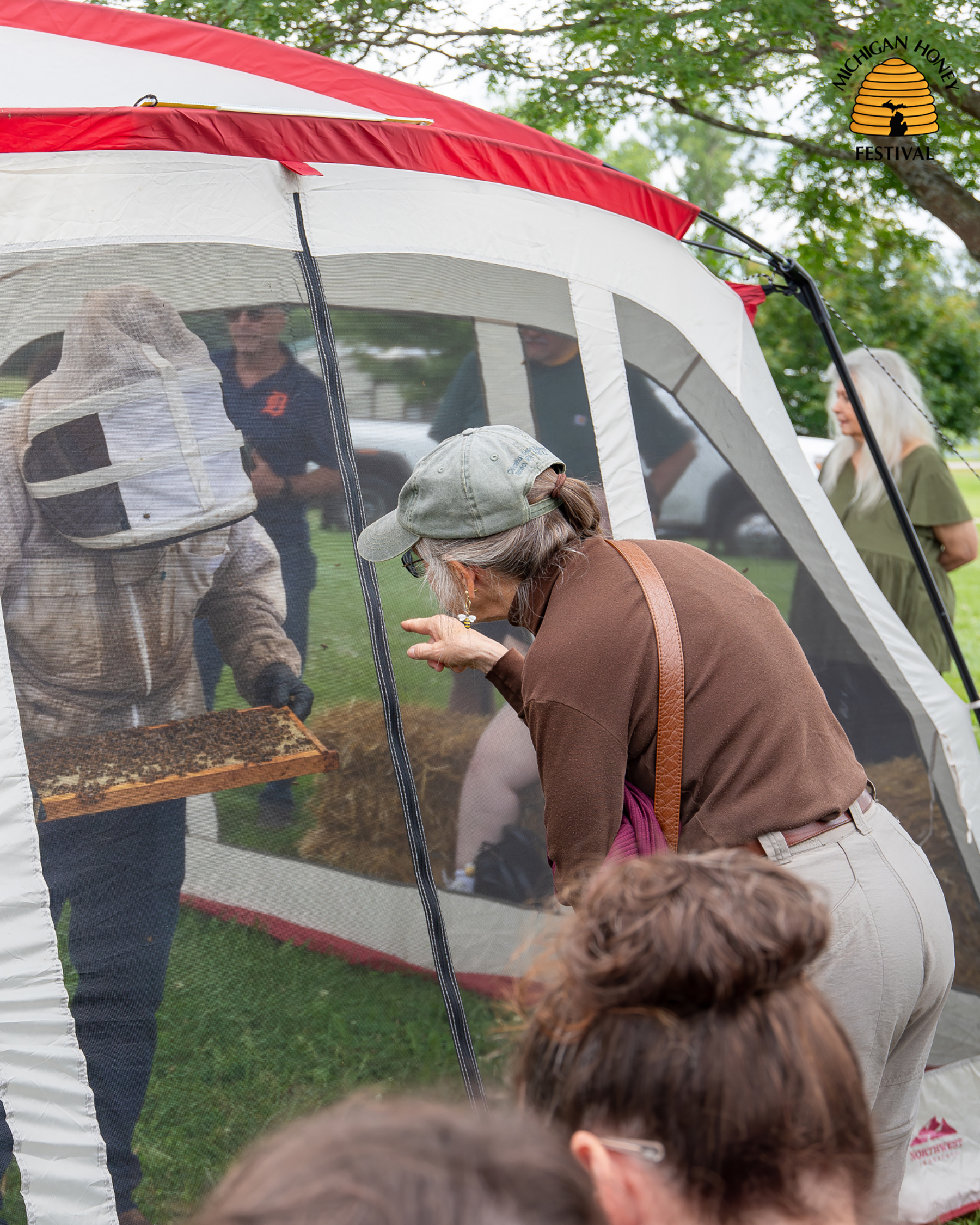 Michigan Honey Festival - Woman watches as beekeeper holds bee hive inside of tent