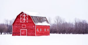 Barn with white trim in white winter landscape and bare trees in the background