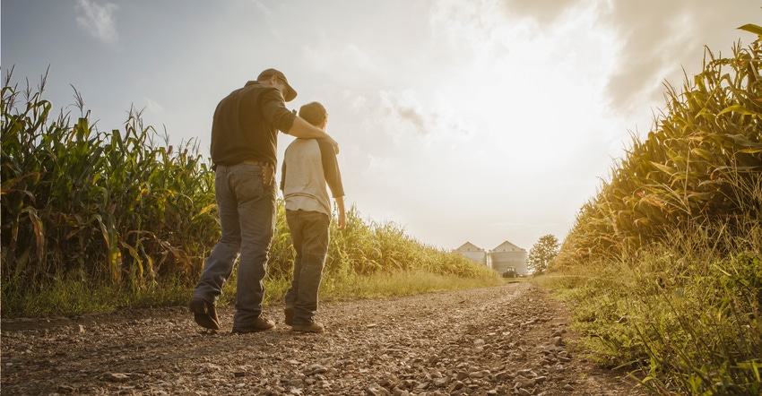 Father and son walking on dirt road through farm