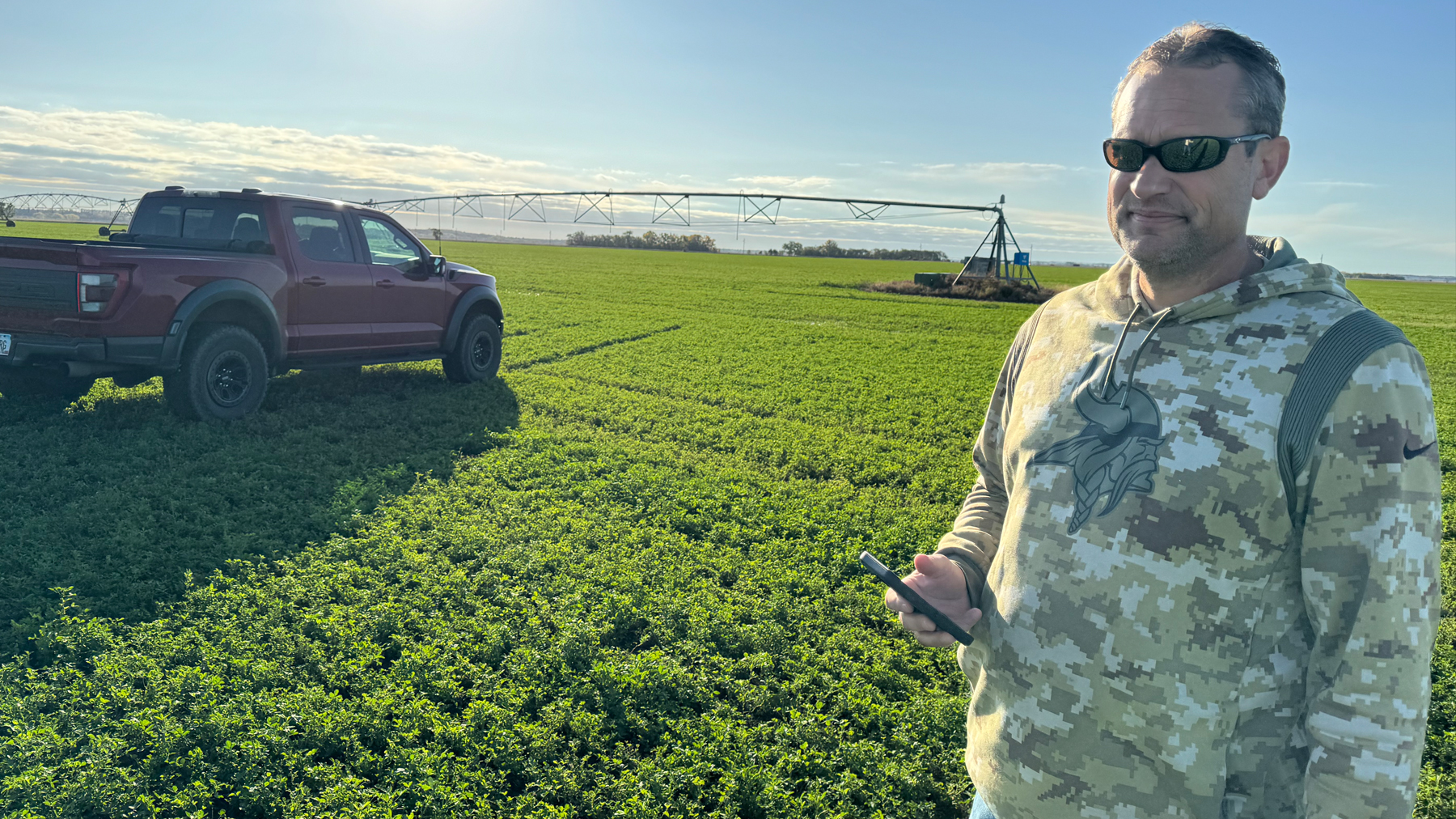 Jory holding smartphone in field with truck and irrigation equipment in background