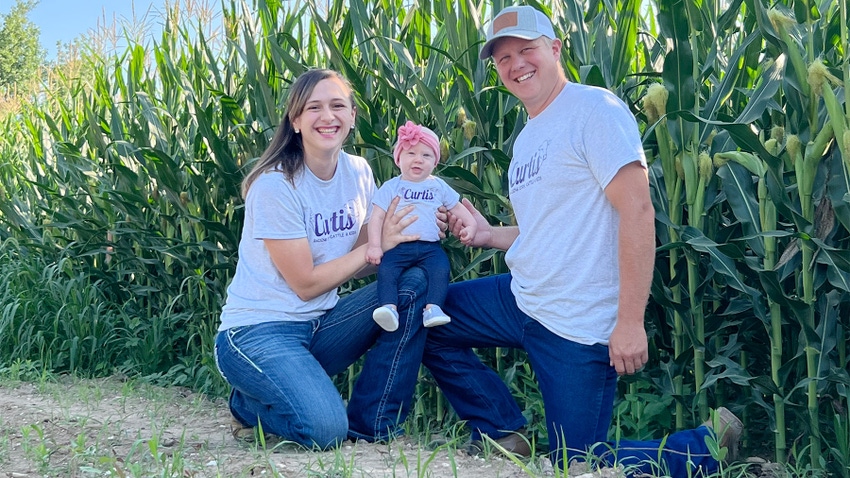 Jeana Curtis with her husband and baby kneeling in a crop field