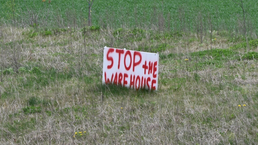 spray-painted "STOP the warehouse" sign staked in the ground