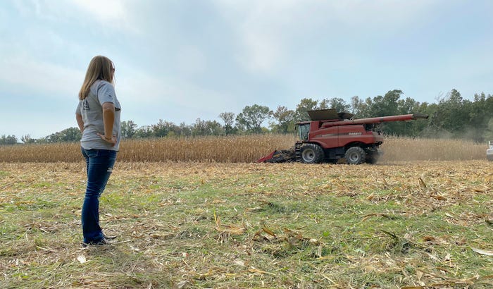 Woman watches combine on farm.