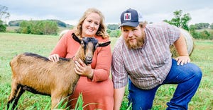Heidi and Jason Benson, owners of Lymett Goat Farm, pose with a goat in open pasture