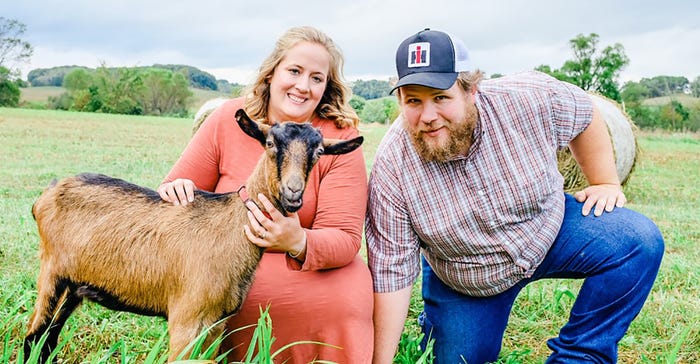 Heidi and Jason Benson, owners of Lymett Goat Farm, pose with a goat in open pasture Heidi and Jason Benson, owners of Lymett Goat Farm, pose with a goat in open pasture