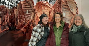 Heather Oppor, April Prusia, and Heidi Hoff stand in front of hanging meat carcasses
