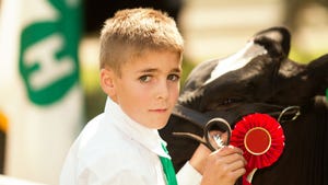 A young boy with a red ribbon and a Holstein cow
