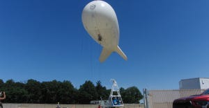 A white, balloon-like aircraft tethered by string as technicians position it for launch
