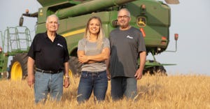 Three generations of farmers pose in the middle of a field with a green tractor behind them