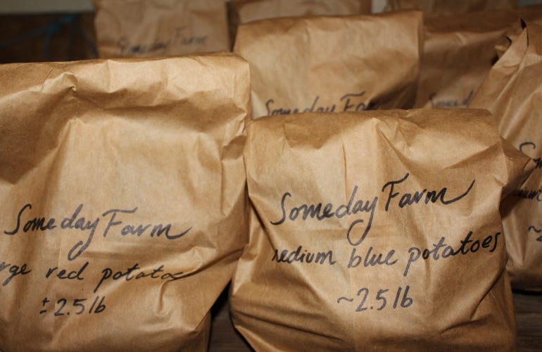 Potatoes in brown paper bags with handwritten labels await customers at Someday Farm's self-serve store