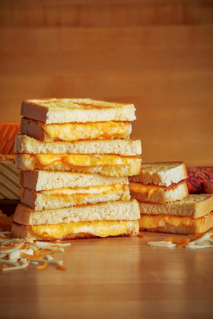 Stacked grilled cheese sandwiches sliced in half with cheese oozing out
