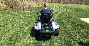 view of boy mowing lawn on riding lawnmower from behind him