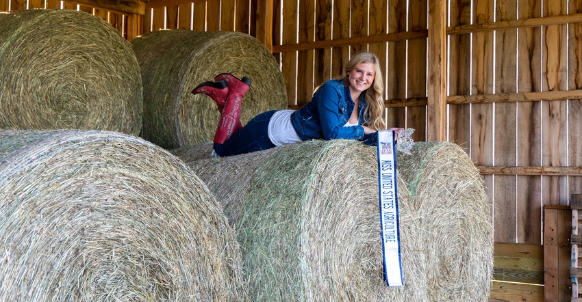 Bella Monroe lying on top of big round hay bales inside a barn