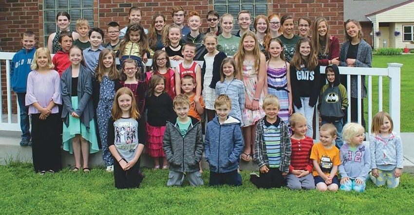 A large group of kids of various ages pose for a photo in front of a brick building