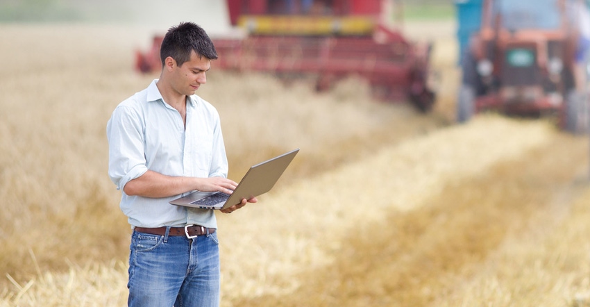 young farmer with computer in field of wheat