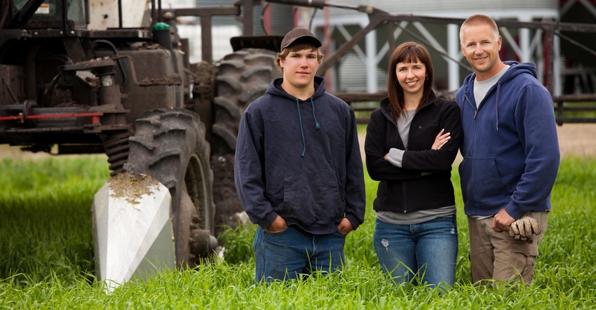 A farm couple stands with their young adult son beside equipment in the field