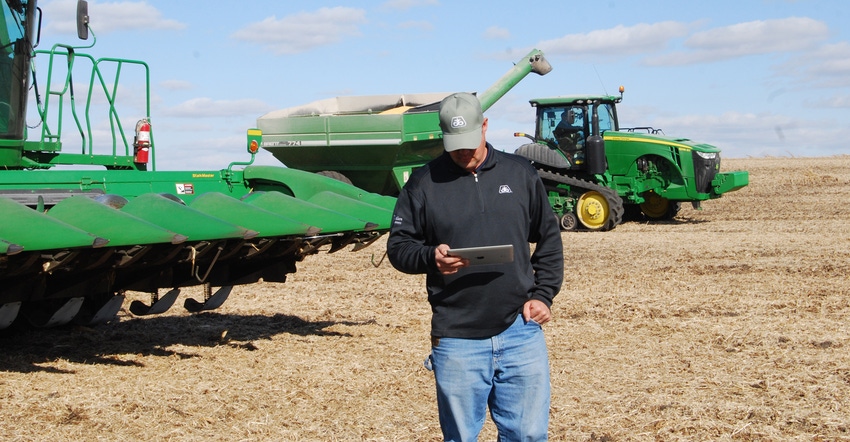 Farmer looking at tablet in field with grain auger and combine in background