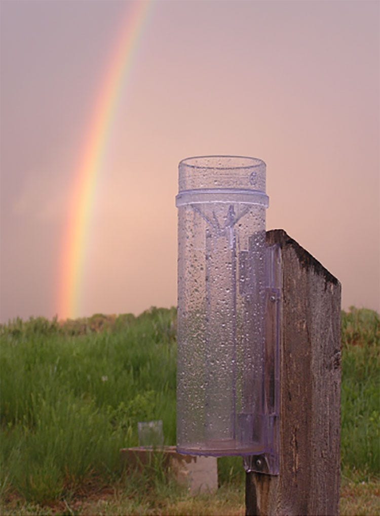 A rain gauge in a field with a rainbow in the background