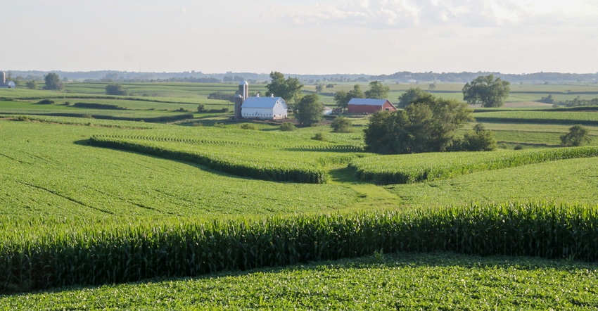 A wide landscape of a crop field with a barn far in the distance