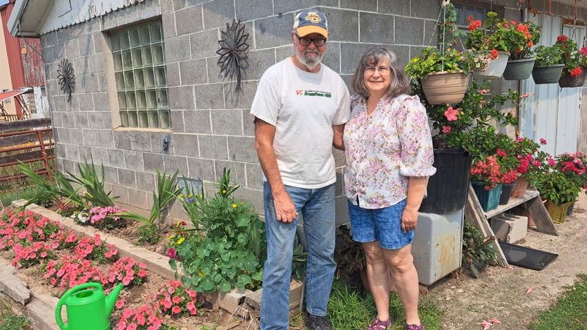 husband and wife standing in front of house and next to flowerbeds