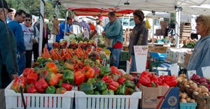 Farmers look on as customers shop tables of fresh vegetables at a farmers market