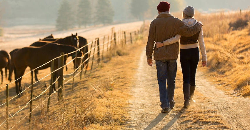 young couple walking away, arm in arm, on country road with cattle off to the side