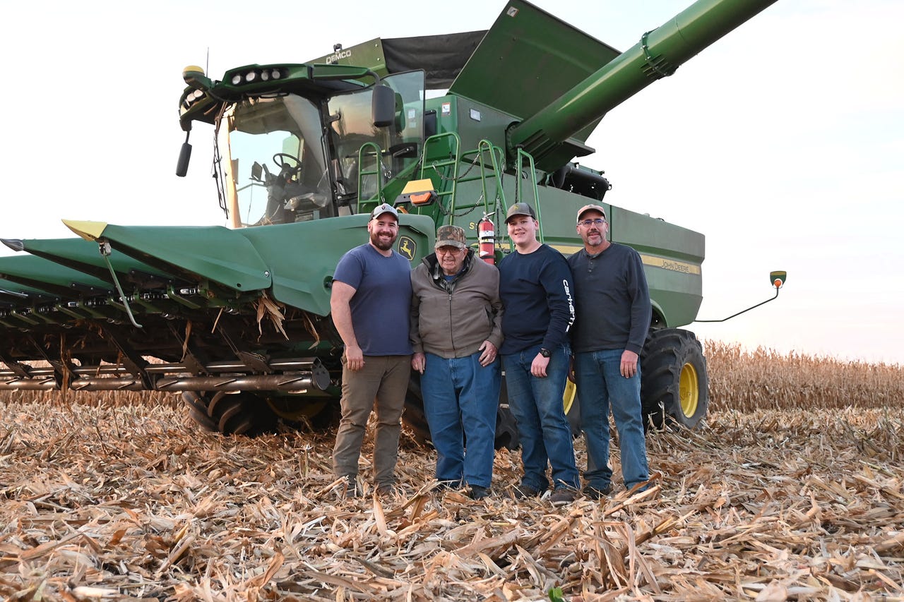 4 men pose in front of combine during corn harvest