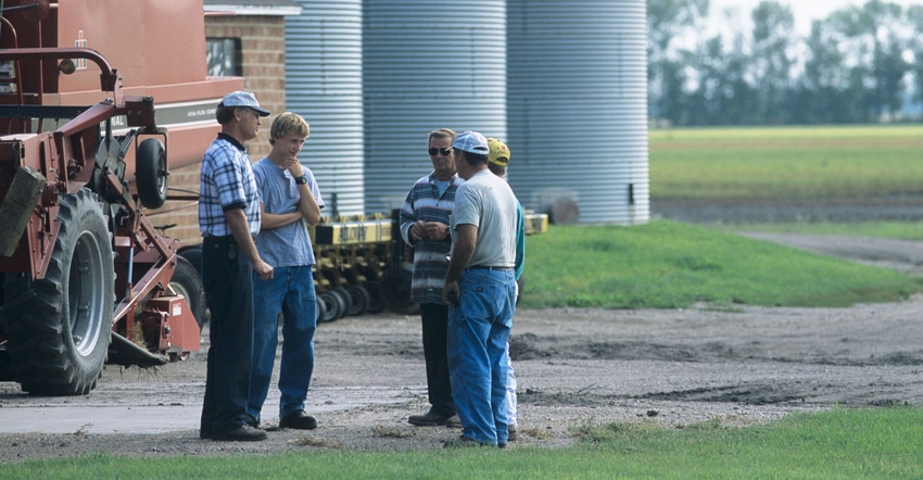 Farmer and hired hands talking near combine on farm