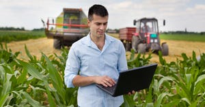 young man with laptop in a field with harvest equipment behind