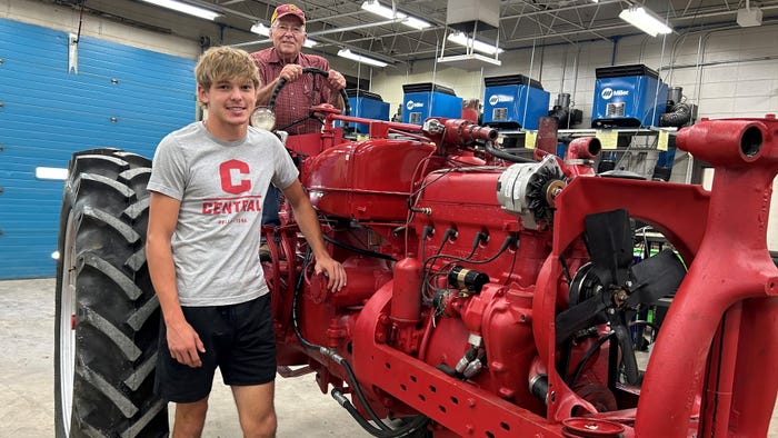 Klayton Bremer stands beside the tractor owned by his grandfather who is sitting on it