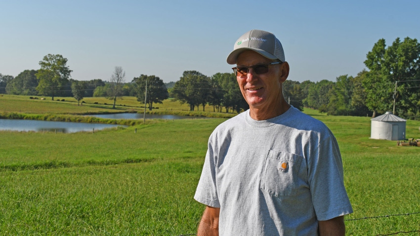Man wearing cap standing with farm in the background.