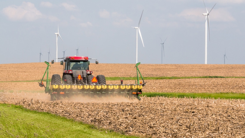 Planting corn in field with wind turbine in background