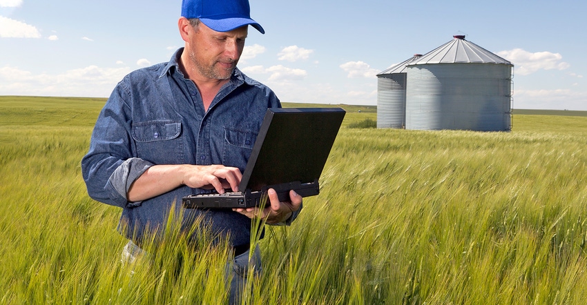 farmer standing in wheat field with laptop computer