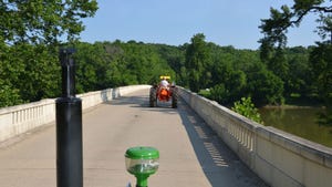 view of a vintage orange tractor crossing a bridge in a forested area