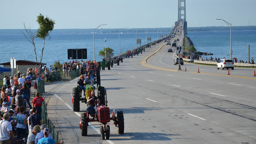 A parade of tractors crossing a bridge over water