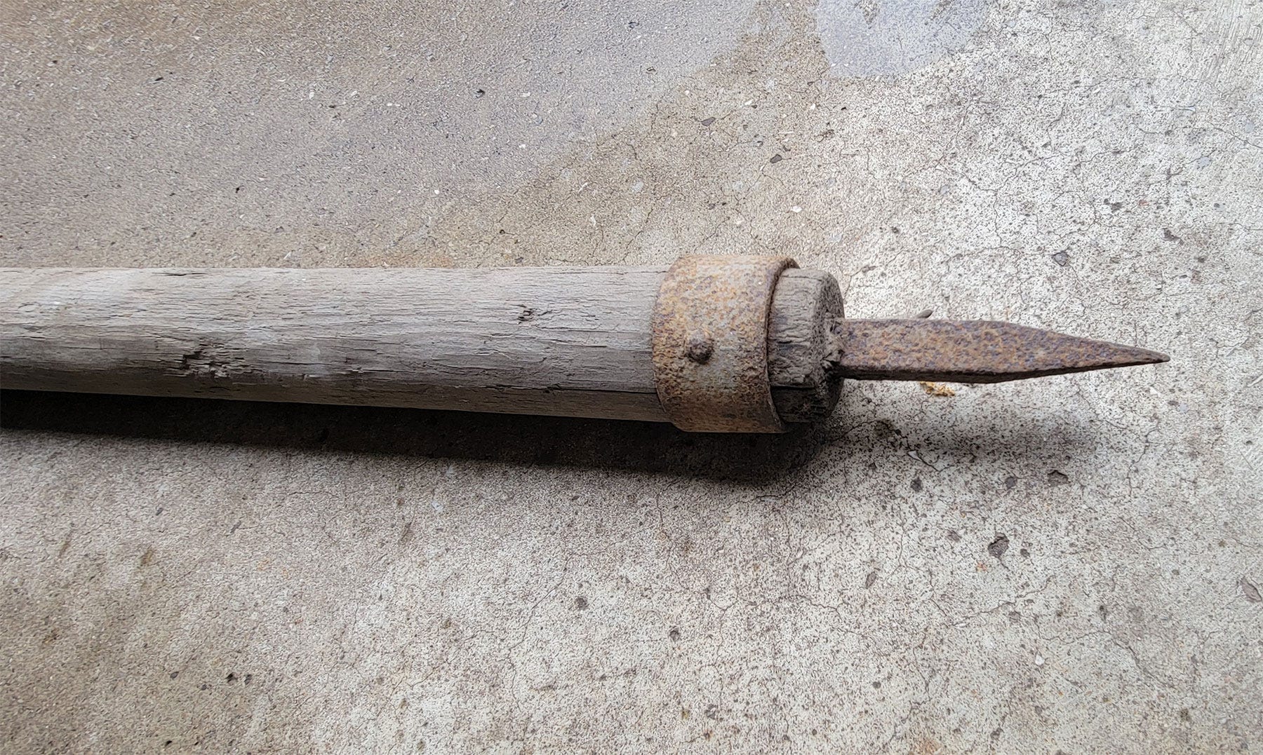 A close-up of an iron arrow attached to a wooden pole