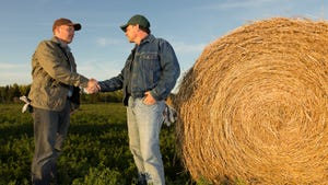 Farmers next to bale of hay shaking hands