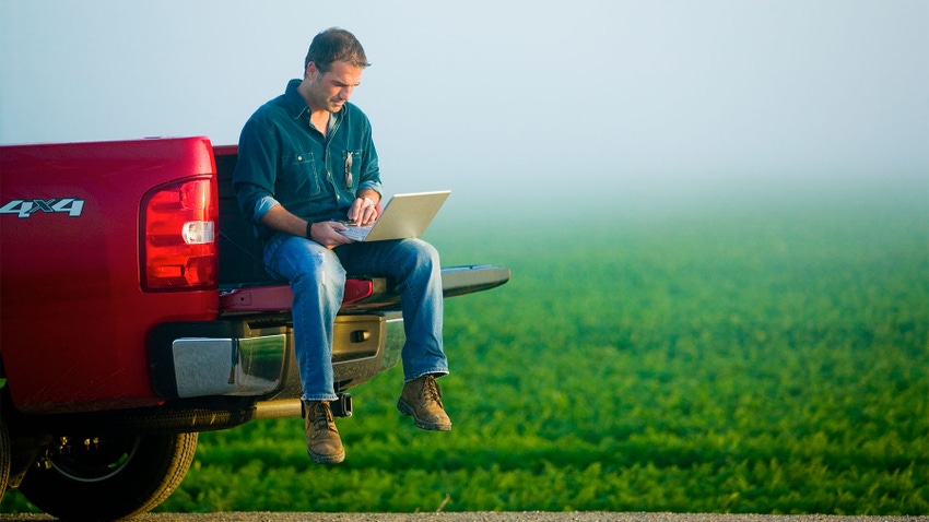 A farmer sitting on the tailgate of a pickup truck and using a laptop