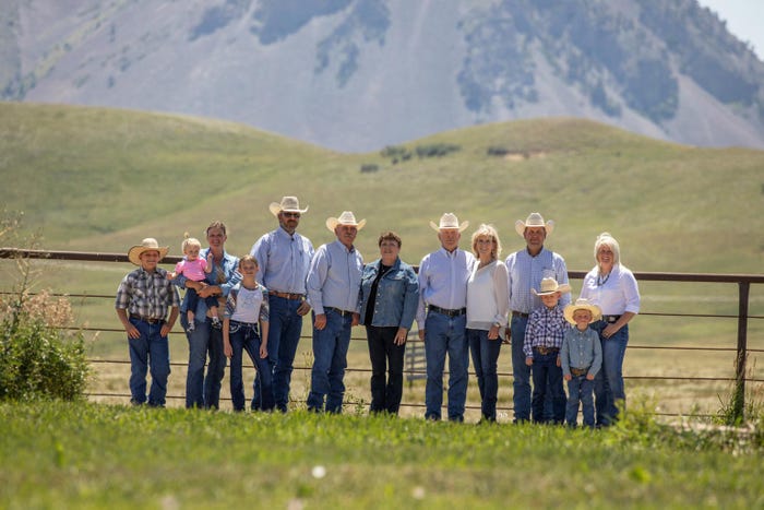 A family portrait, a group of people of varying ages standing in front of a metal fence with mountains in the background