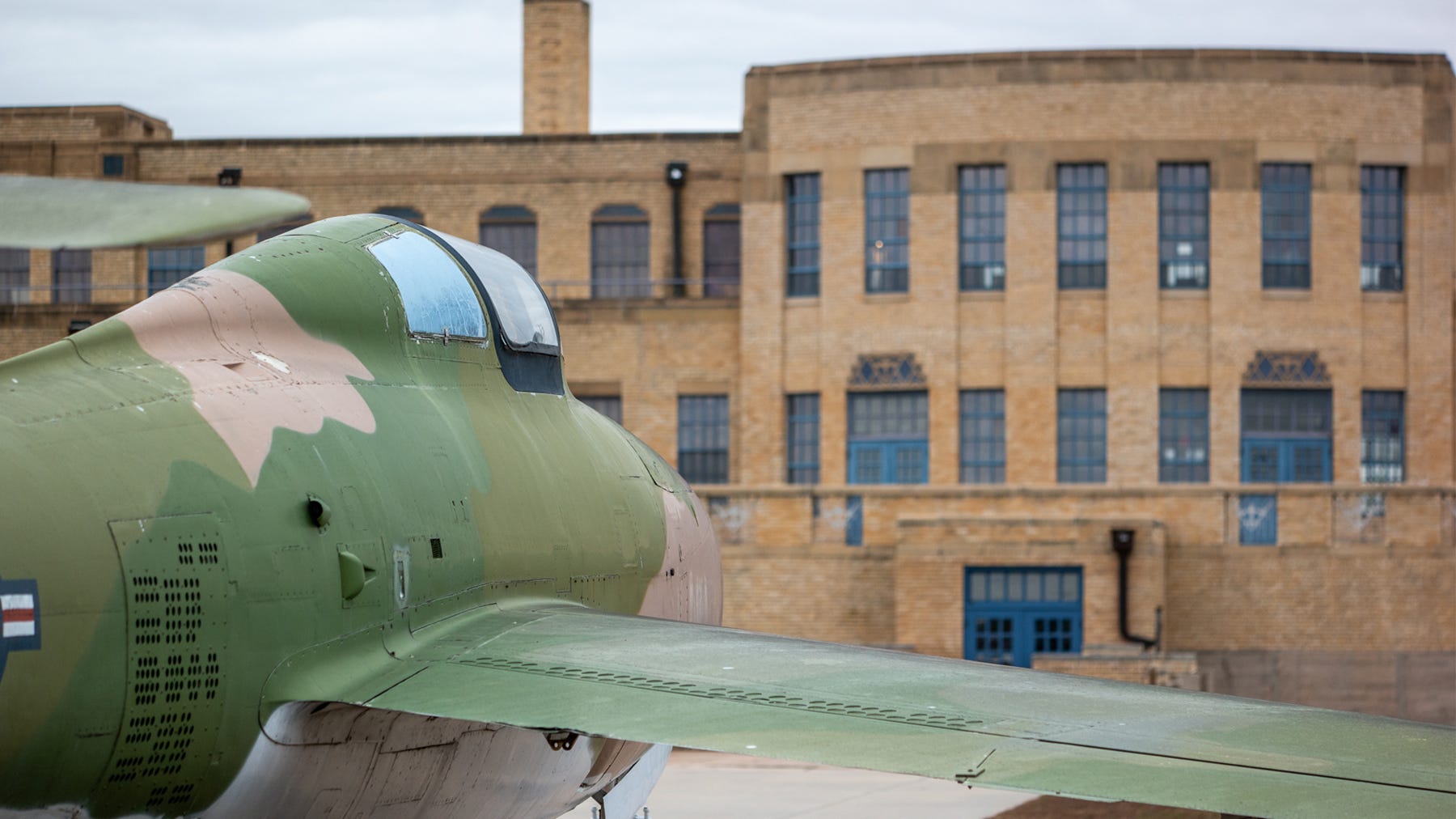 camouflage-painted plane outside old airport building