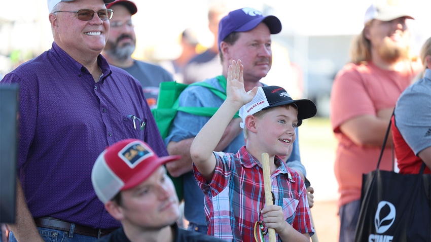 A young boy raising his hand while sitting in a crowd