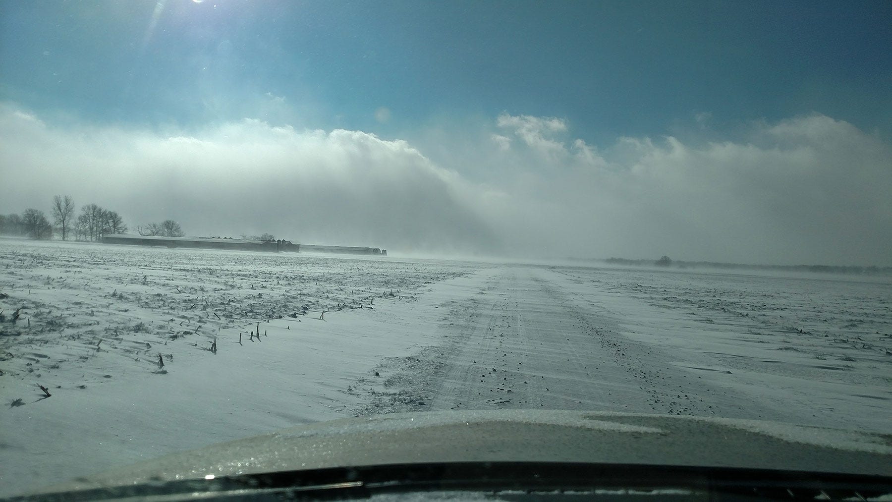 a rural road with snow blowing across it