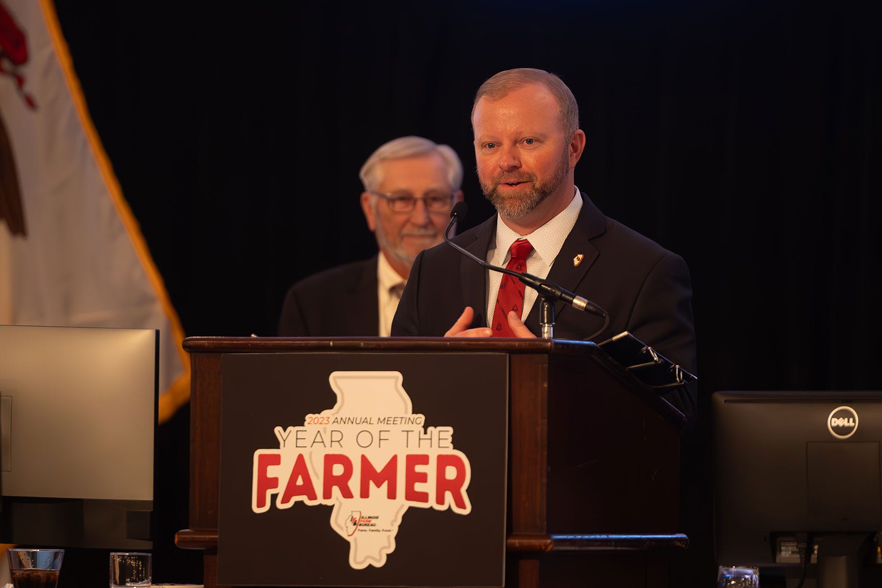 Evan Hultine, the 2023 Illinois Farm Bureau vice president, speaking into a microphone as he stands behind a podium
