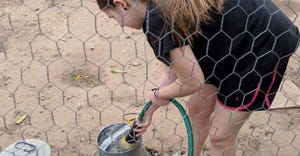 Girl in chicken coop filling up pail with water hose