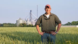 Young farmer in field in front of silos
