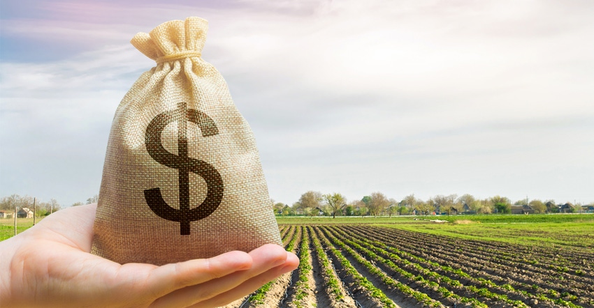 Hand holding bag of money with field of crops in background