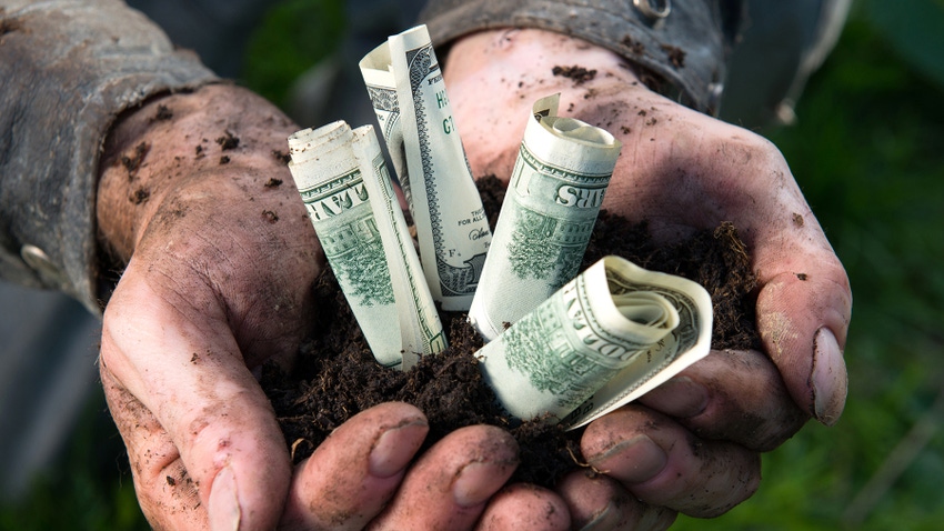 Hands holding soil with rolled up paper bills