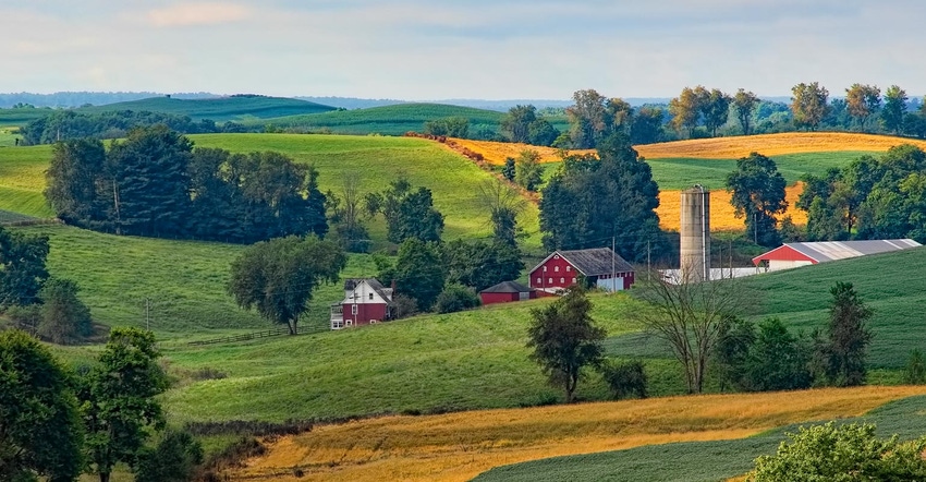 A farmstead with a red barn and house surrounded by fields and hills