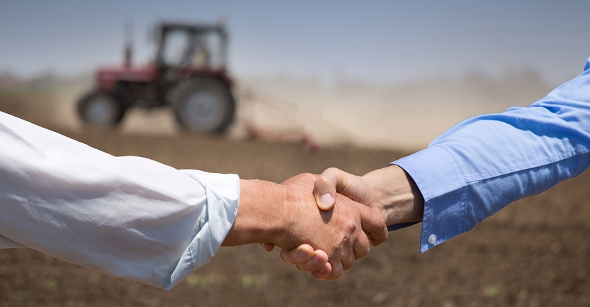 Two people shaking hands with tractor in background
